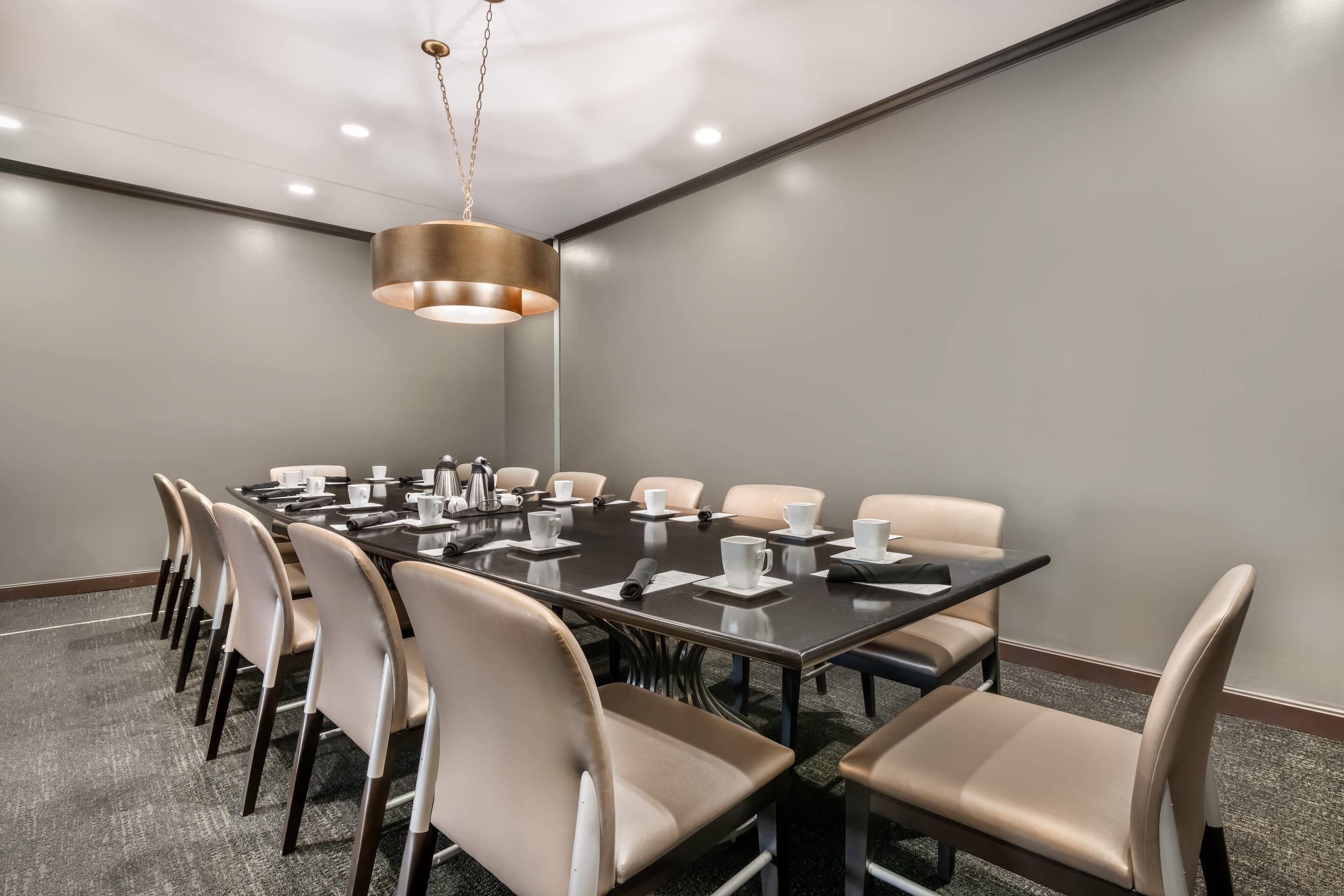 A conference room with a long table, chairs, a coffee pot, and a hanging light fixture.
