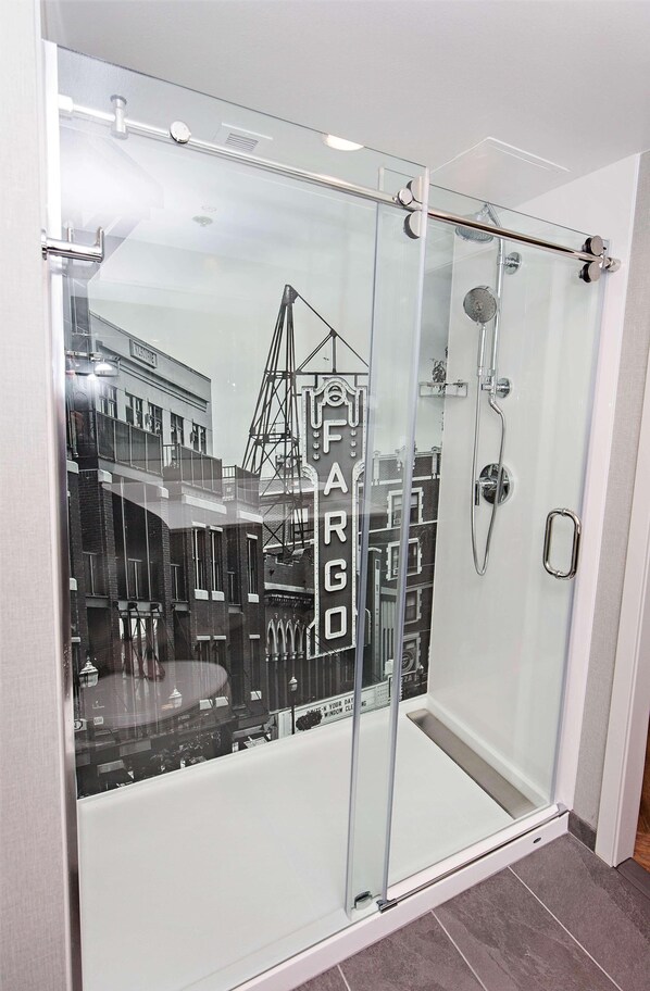 A modern shower with a glass door, a handheld showerhead, and a control panel.