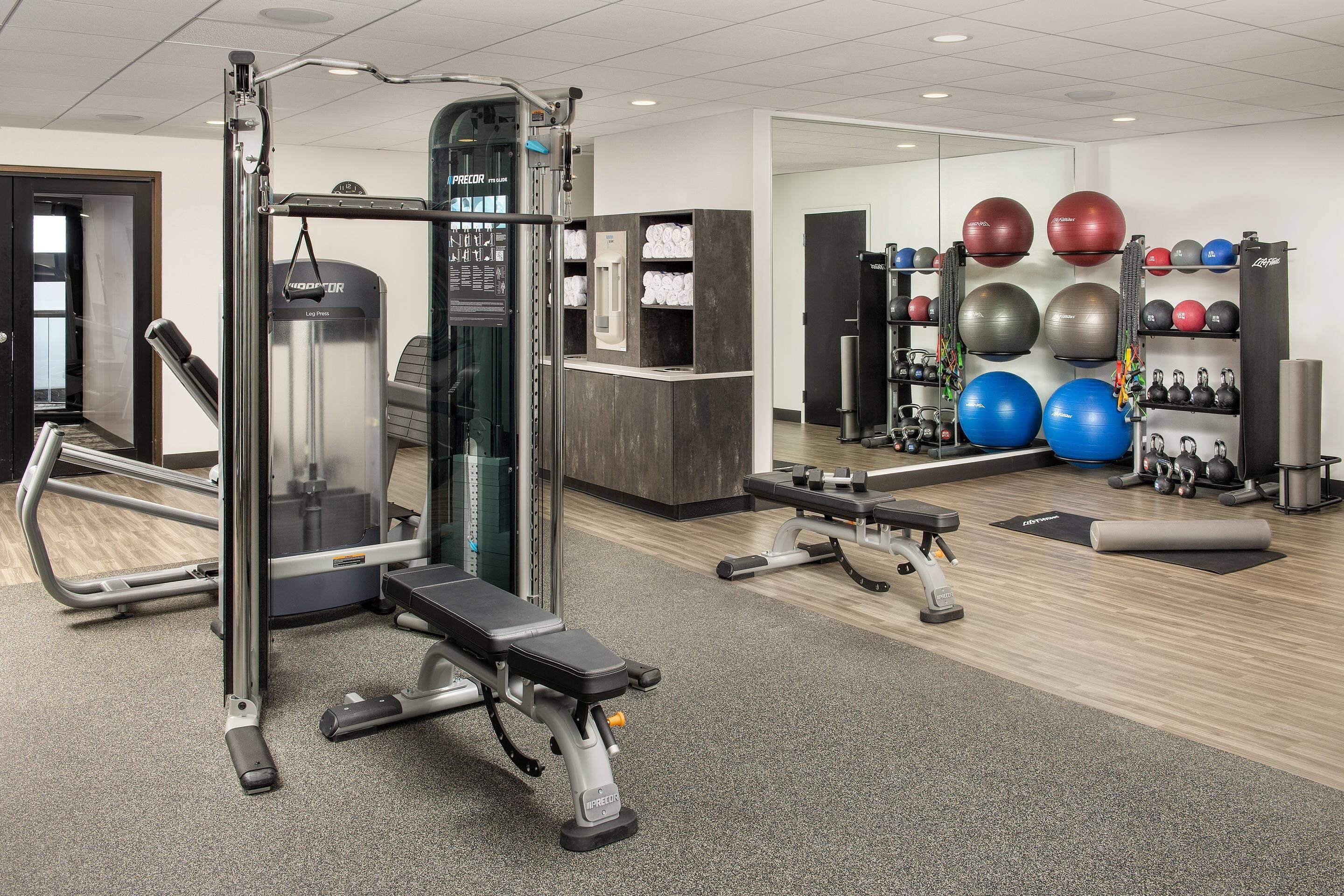 Une salle de sport équipée de matériel d’exercice, d’un tapis de course et d’un mur recouvert de ballons d’exercice.