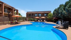 A swimming pool with lounge chairs and umbrellas, surrounded by a fence and a building with balconies.