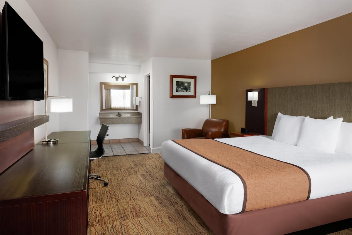 A hotel room with a bed, a desk, a chair, a television, a mirror, and a bathroom with a sink and towel rack.