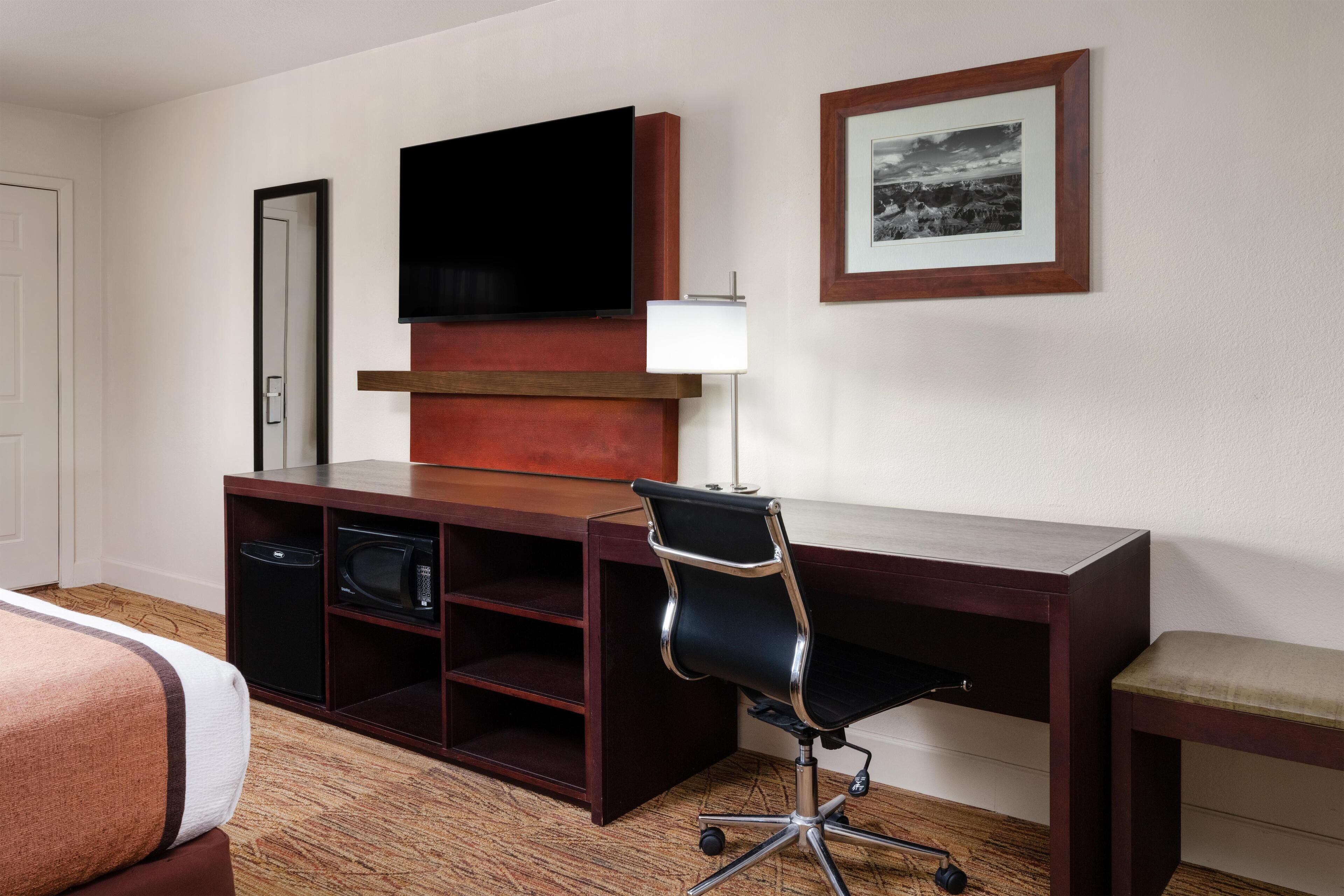 Een hotelkamer met een houten bureau, een zwarte bureaustoel, een televisie, een lijst met een afbeelding en een magnetron.