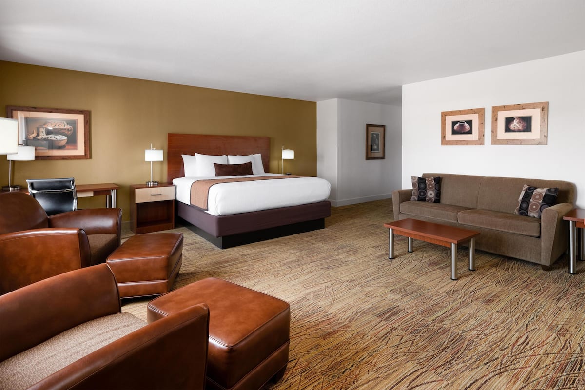 A hotel room with a bed, a sofa, a chair, a coffee table, and a desk with a lamp.