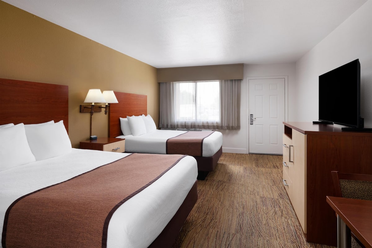 A hotel room with two beds, a television, a desk, and a window with curtains.