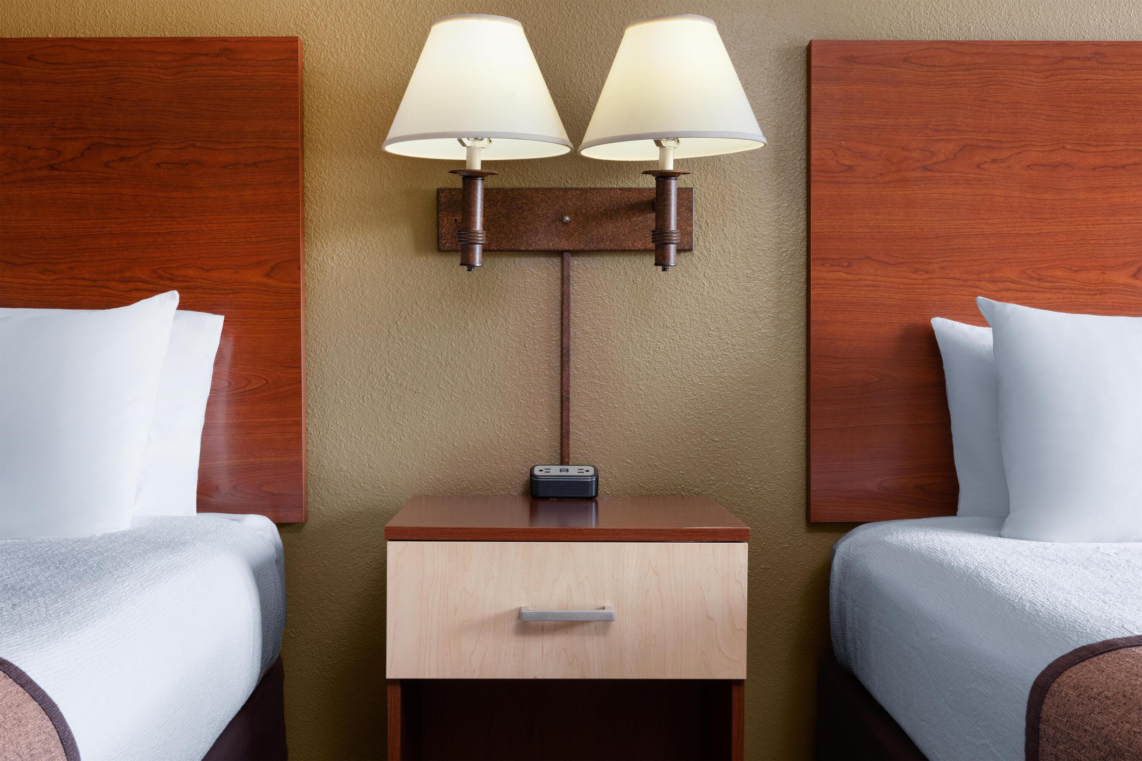 Une chambre d’hôtel avec deux lits, une table de chevet avec une lampe et un petit tiroir.