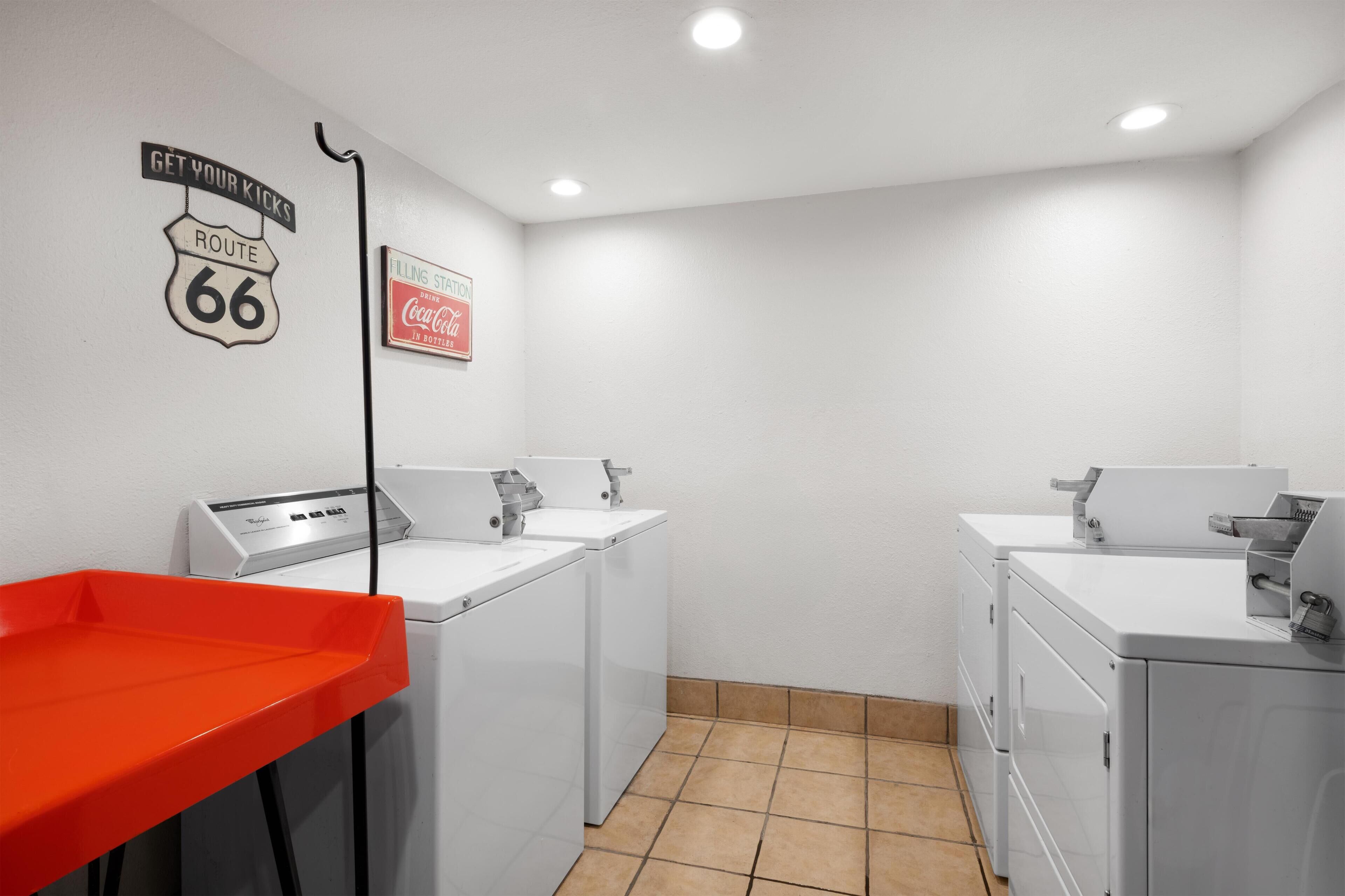 Un cuarto de lavandería con dos lavadoras, un lavamanos rojo y carteles en la pared.
