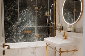 A bathroom with a bathtub, a sink, a mirror, and a shower area with a glass door. - Castle Hotel Windsor (Windsor)