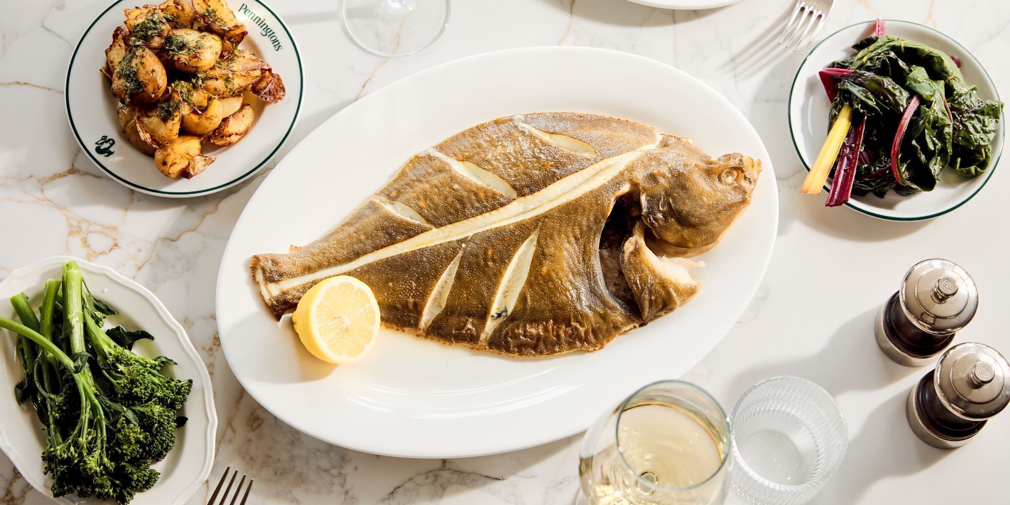 Une table à manger avec un poisson, des brocolis et une tranche de citron.