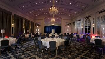 A banquet hall with round tables, chairs, a chandelier, and a stage.