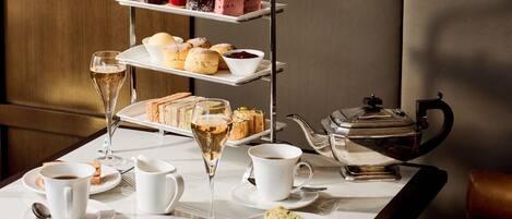 A three-tiered dessert tray with various pastries and a teapot on a table.
