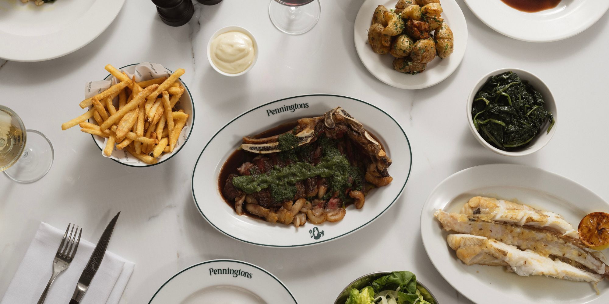 Mesa dispuesta con diferentes platos, incluyendo pescado, papas fritas y verduras, indicando un ambiente para comer.