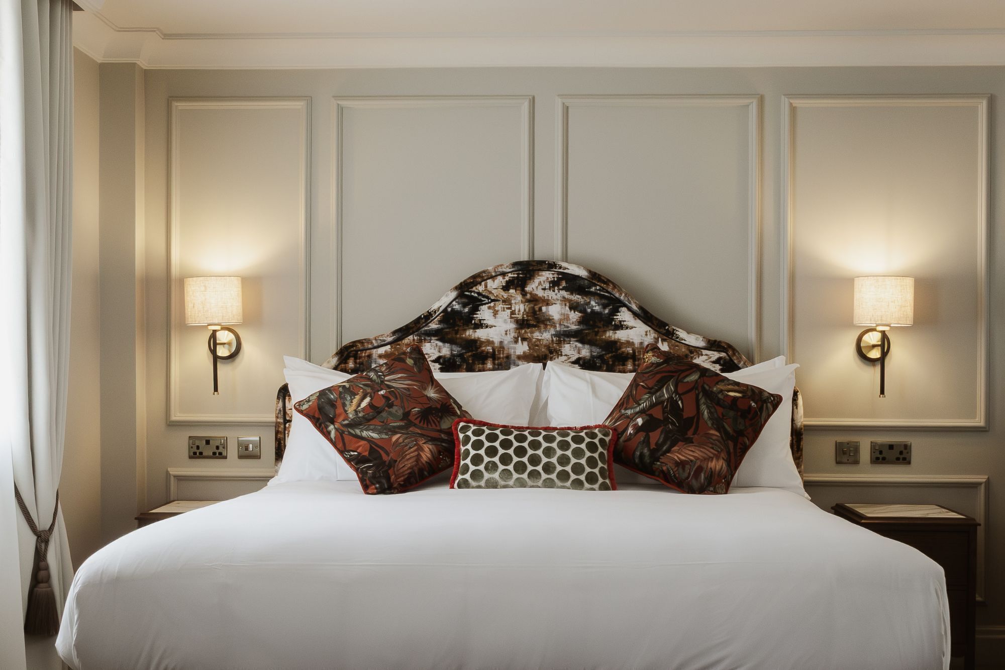 A hotel room with a large bed, two wall-mounted lamps, and a headboard with a floral pattern.