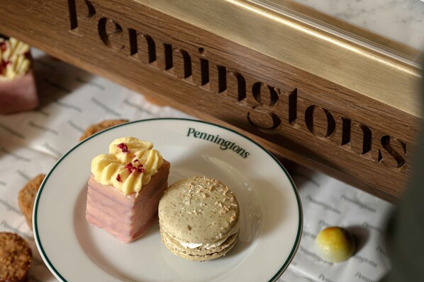 A plate with a pastry and a biscuit, a wooden sign with the word 'Penningtons,' and a blurred background with more pastries. - Castle Hotel Windsor (Windsor)