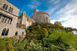 A historic stone building with arched windows and a round tower, surrounded by lush greenery. - Castle Hotel Windsor (Windsor)