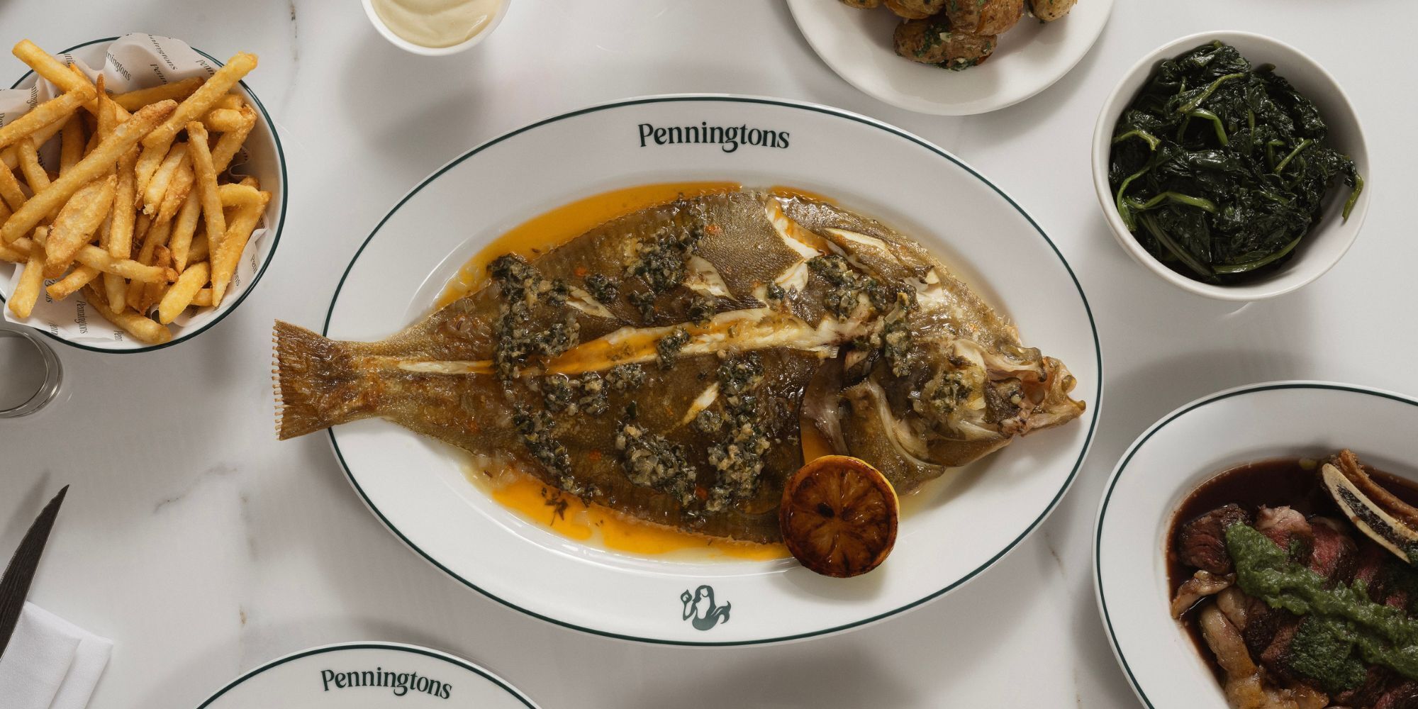 Uma mesa de jantar com diversos pratos, incluindo um peixe inteiro, batatas fritas e salada.