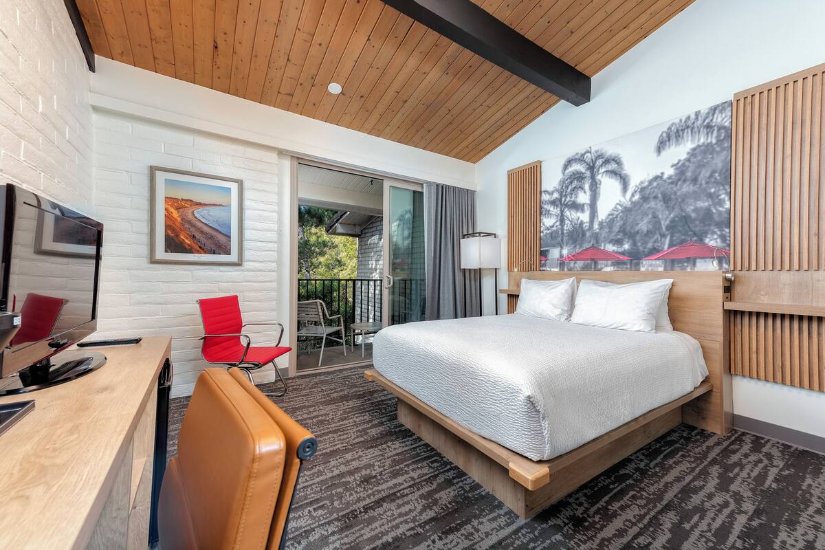 A modern hotel room with a bed, desk, chairs, and a TV.