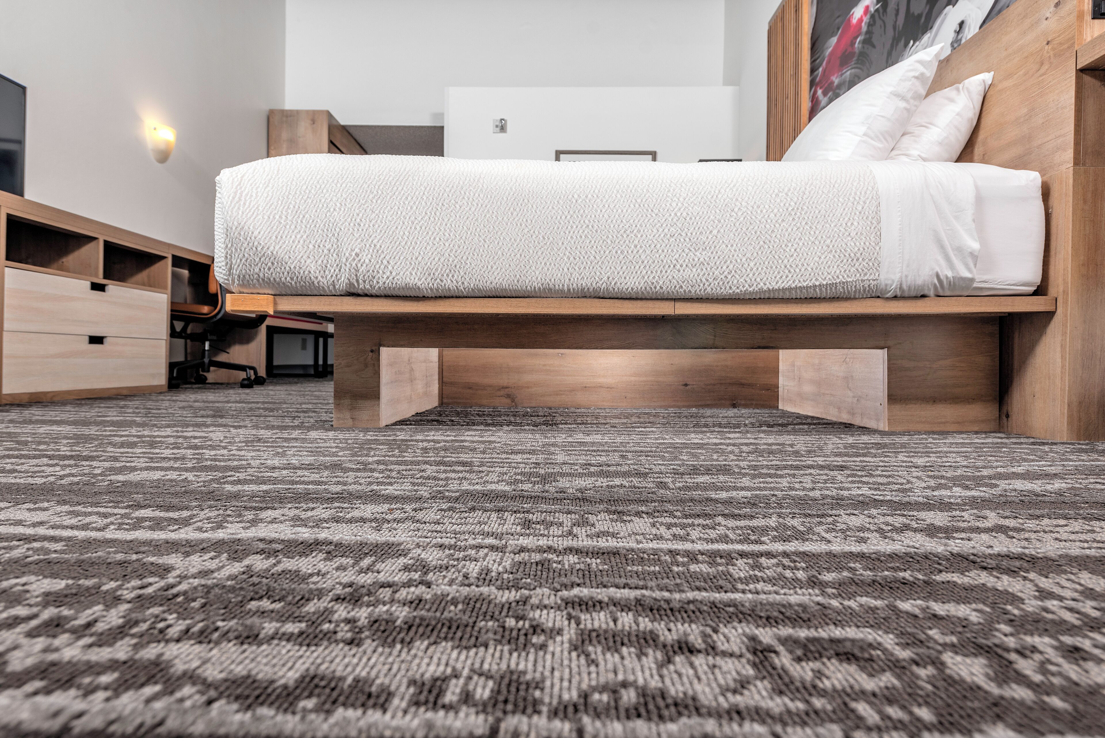 Een moderne slaapkamer met een laag bed, ingebouwde opbergruimte en een kamerbreed tapijt met dessin.