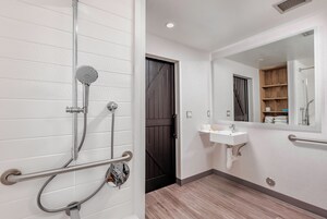 Un baño con ducha, lavamanos, espejo y una puerta con panel de madera.