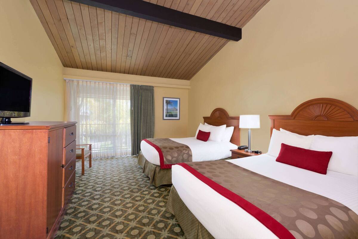 A hotel room with two beds, a wooden headboard, a television, a desk, and a patterned carpet.