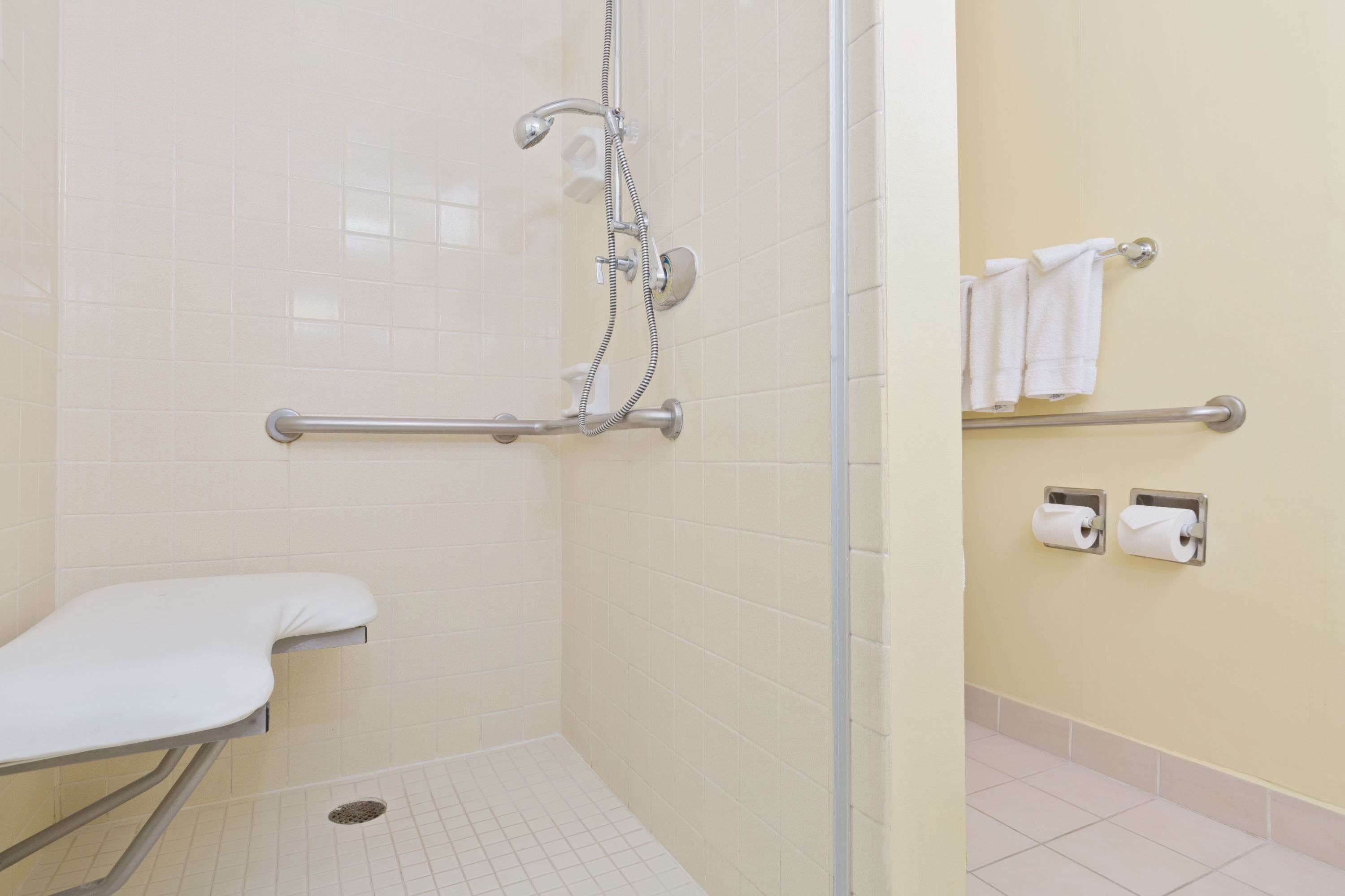 A bathroom with a shower, grab bars, a toilet, and hand dryers.