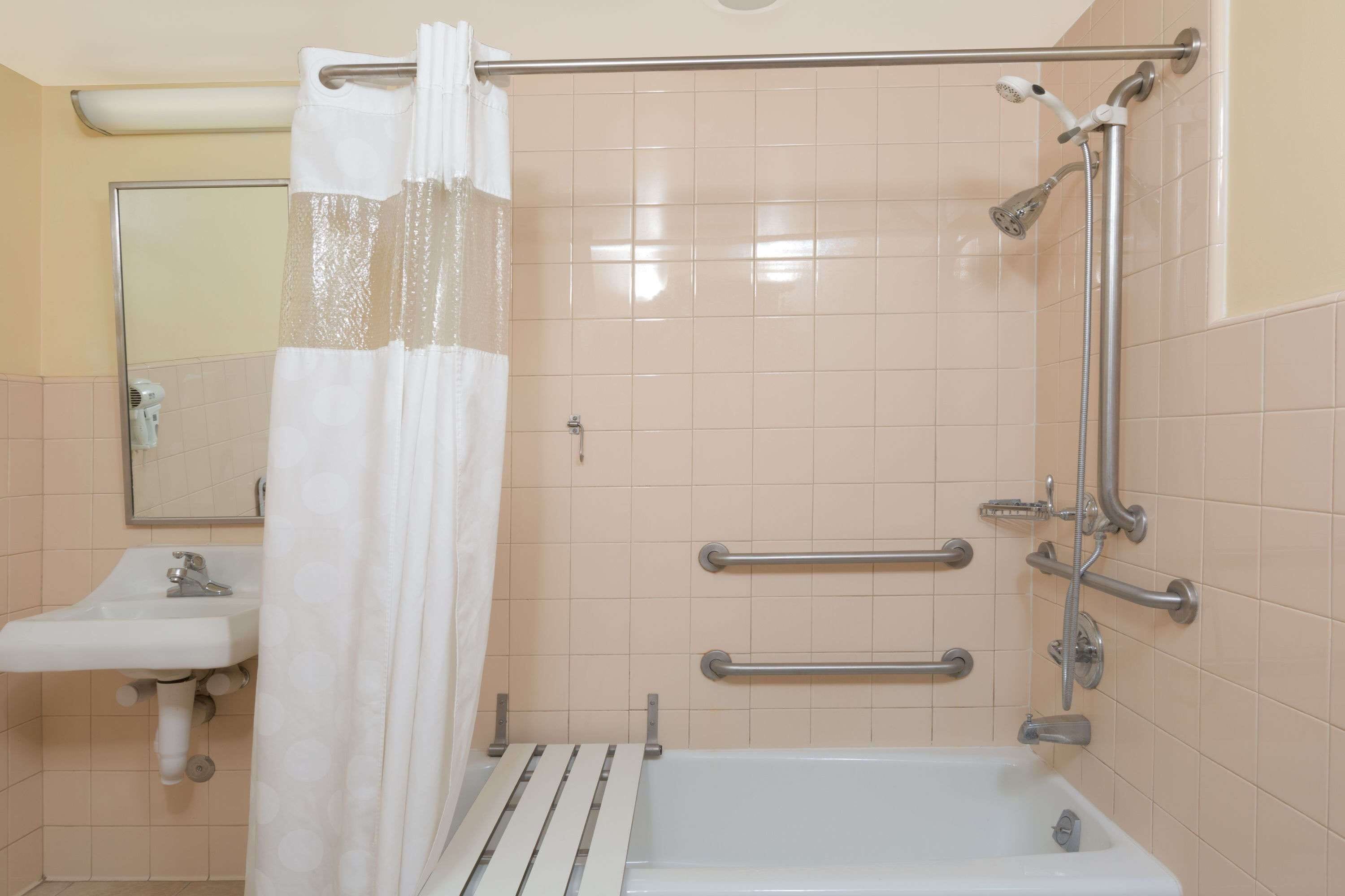 A bathroom with a bathtub, a sink, a shower with grab bars, and a mirror.