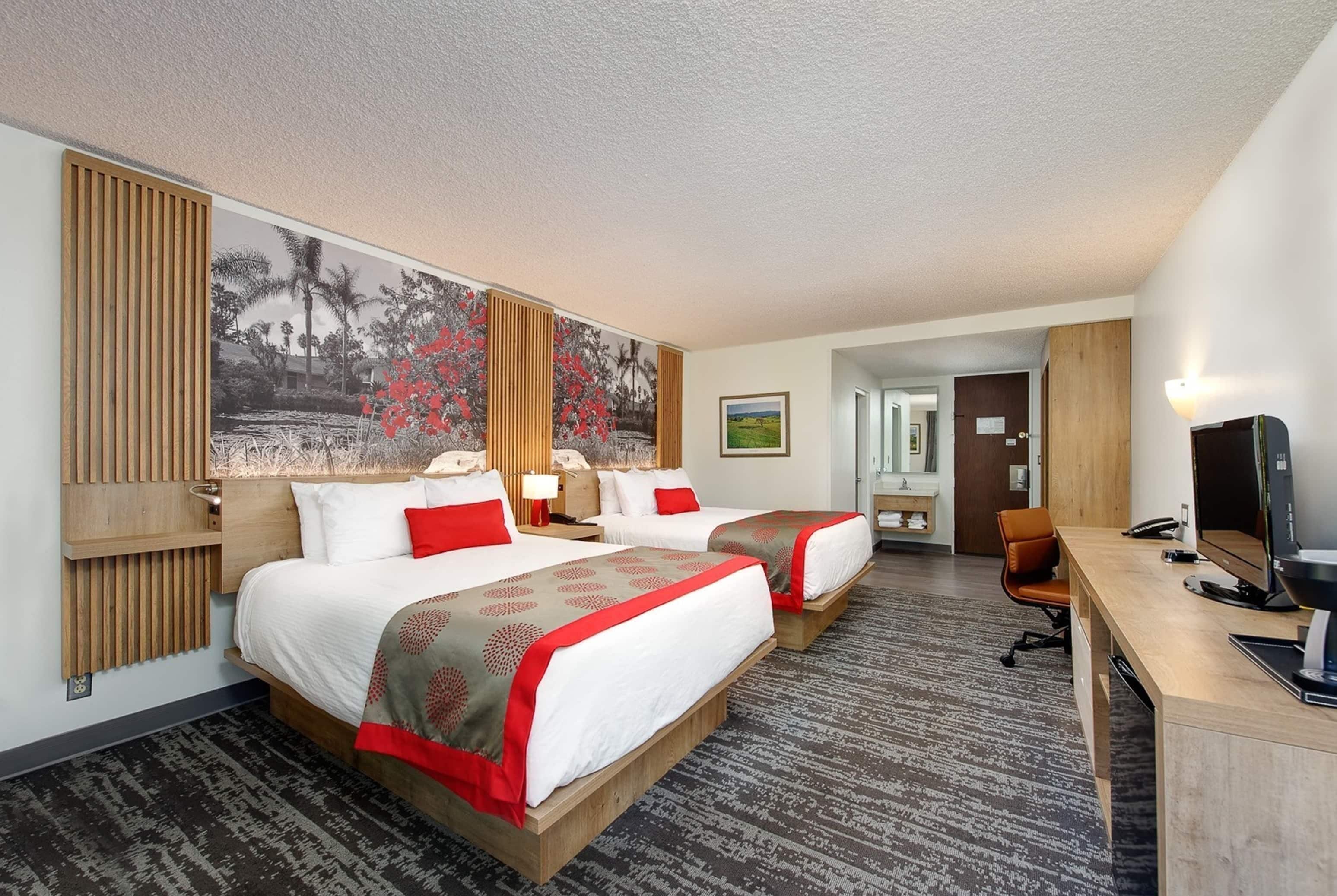 A hotel room with two beds, a desk, a TV, and a painting on the wall.
