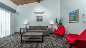 Un salon moderne avec un canapé gris, des fauteuils rouges, une table basse en bois et deux petites tables d’appoint avec des lampes.