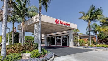 A Ramada hotel with a modern design, featuring a covered entrance and lush landscaping.