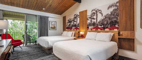 Habitación de hotel con dos camas, un escritorio, una silla y un balcón con sombrillas rojas.