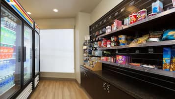 Una tienda de comestibles con estantes llenos de refrigerios y bebidas, una sección refrigerada y un piso de baldosas impecable.