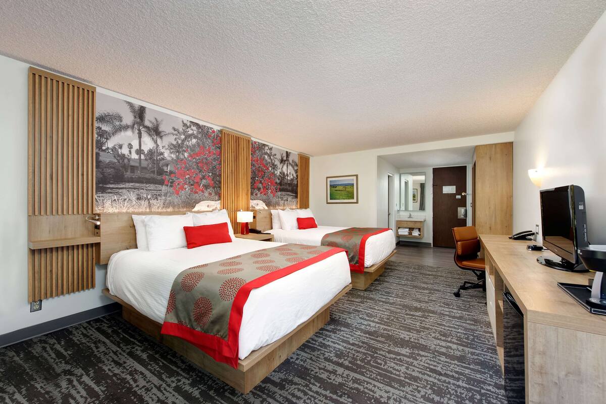 A hotel room with two beds, a desk, a TV, and a large wall mural.