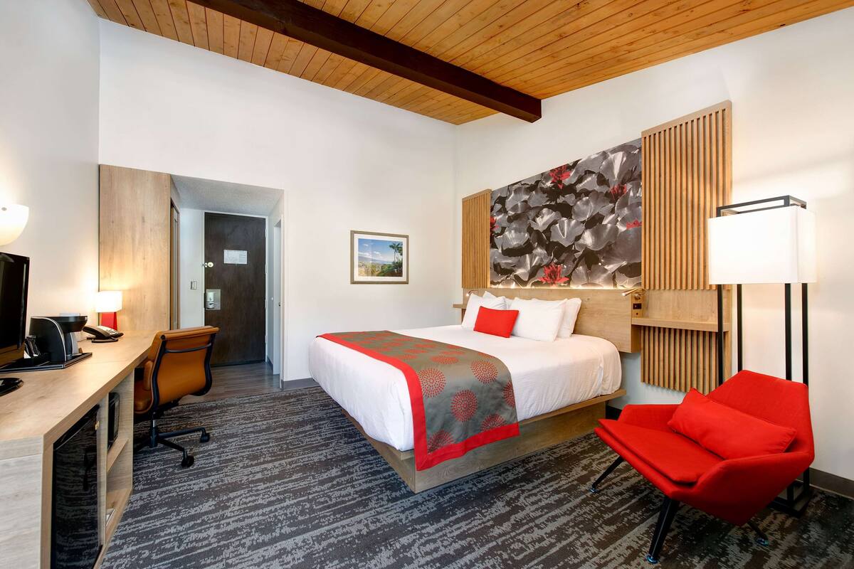 A hotel room with a bed, desk, chair, and a large abstract painting on the wall.