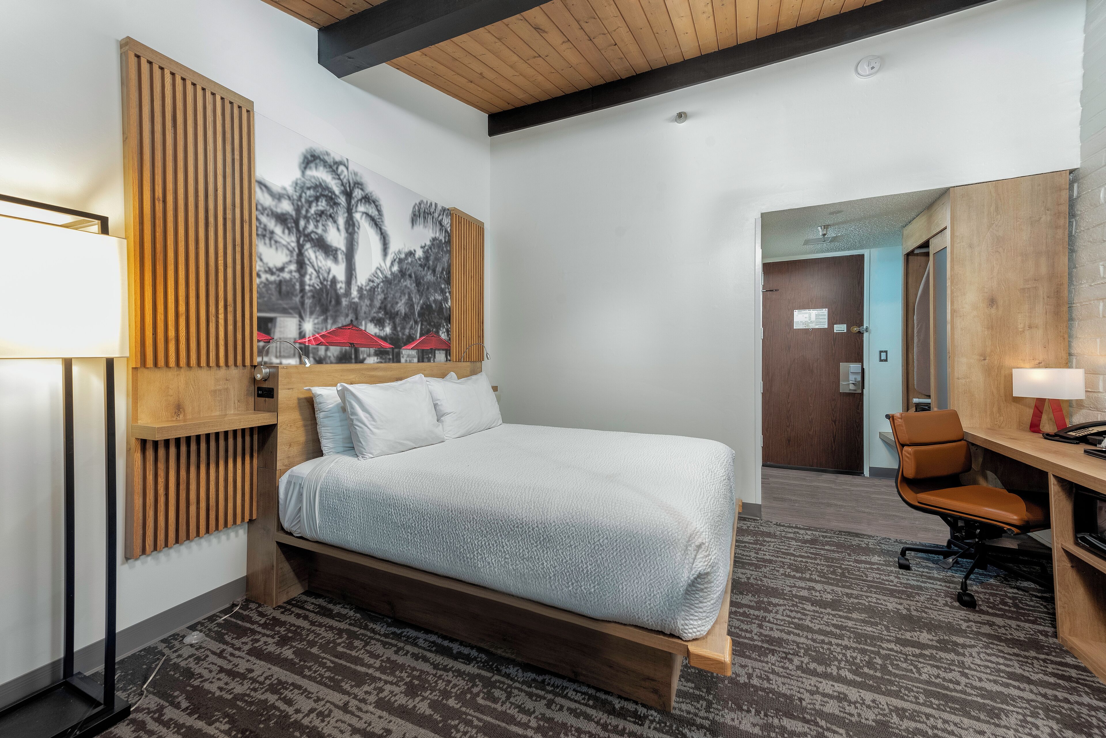 A hotel room with a large bed, a desk, a chair, a lamp, and a wall-mounted radiator.