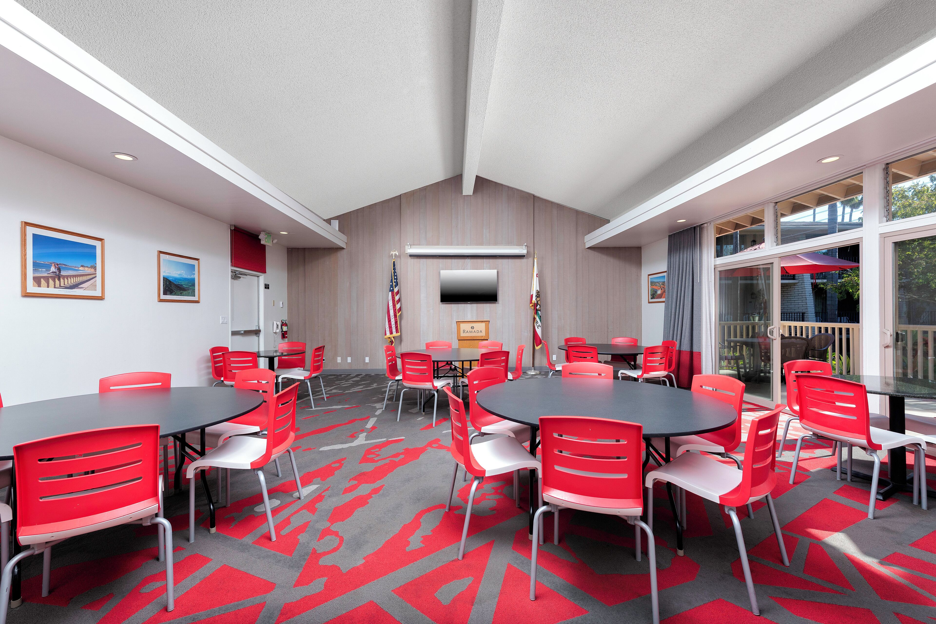 A conference room with red chairs and tables, a flat-screen TV, and flags on the walls.