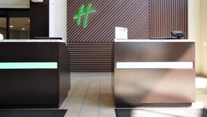 A reception area with two reception desks, a large green logo on the wall, and a modern ceiling design. - Holiday Inn Bloomington - Normal by IHG (Normal)