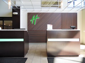 Een receptie met twee balies, een groot groen logo op de muur en een modern plafondontwerp.