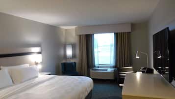 Habitación de hotel con una cama grande, un escritorio, una silla, un televisor y una ventana con cortinas.