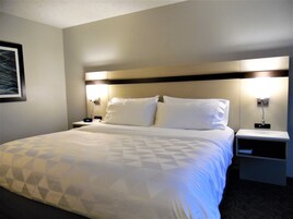 Una habitación de hotel con una cama grande, dos mesitas de noche y una mesita de noche con lámpara.