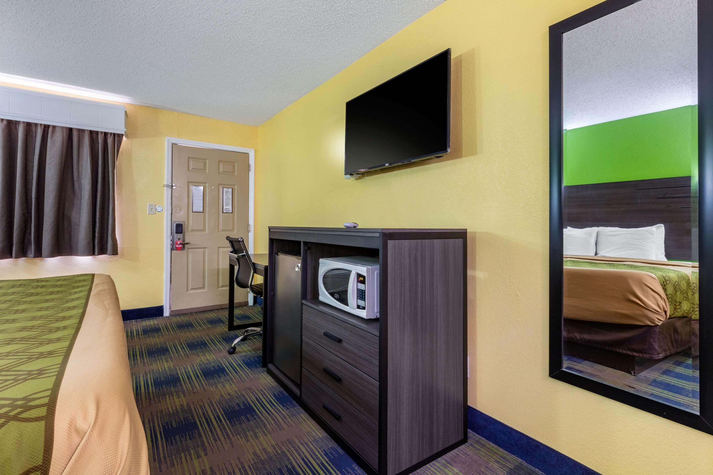 Une chambre d’hôtel avec un lit, un bureau doté d’un micro-ondes, un téléviseur fixé au mur et une porte avec une pancarte.