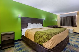 A hotel room with a green wall, a wooden headboard, a bed with white and beige bedding, a nightstand, and a window with curtains.