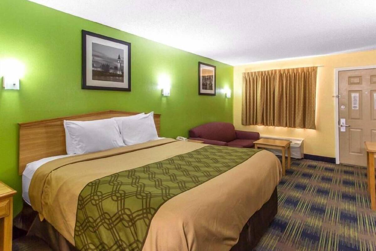 A hotel room with a bed, a chair, a desk, and a door.