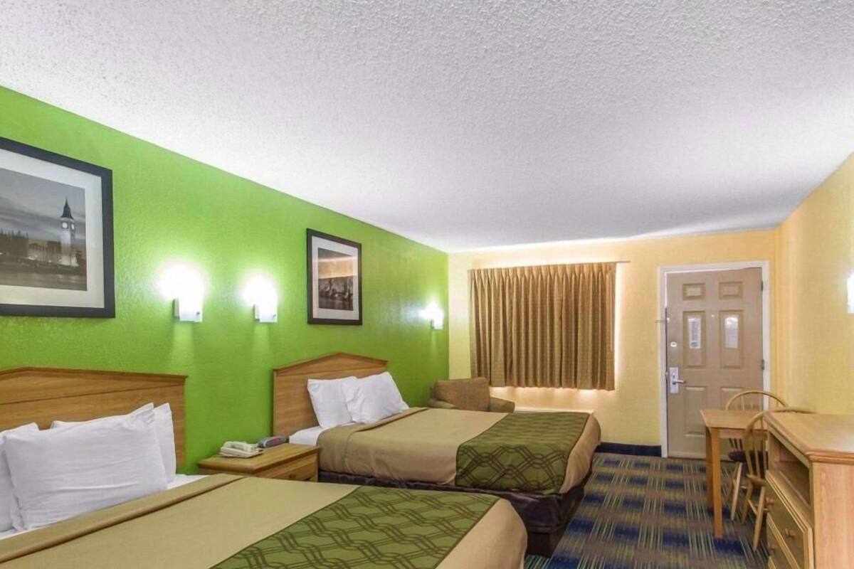 A hotel room with two beds, a desk, a chair, and a door.