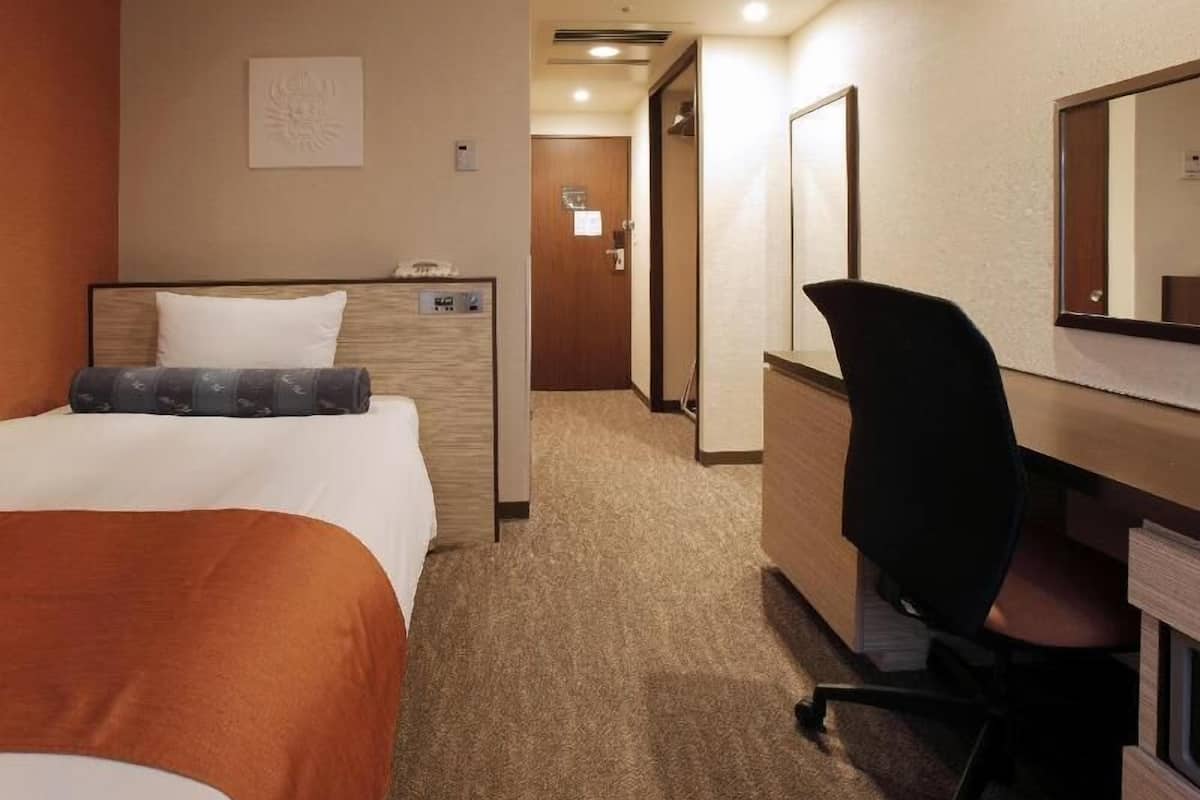 Une chambre d’hôtel comprenant un lit, un bureau, une chaise, un miroir et une porte donnant sur une autre pièce.