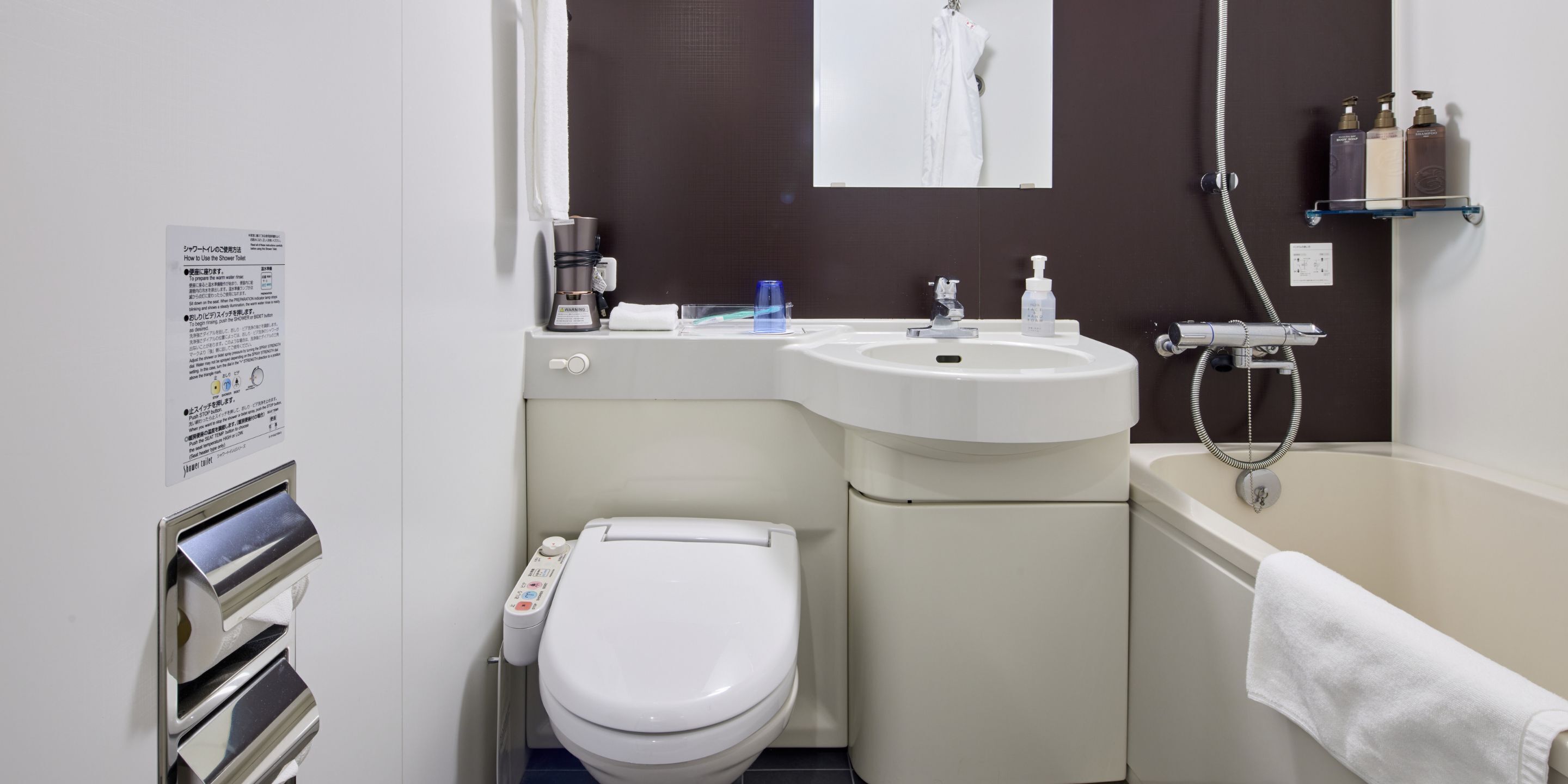 Ein modernes Badezimmer mit Toilette, Waschbecken und Dusche. Ein Handtuch hängt an der Wand, und ein Ablagebereich enthält Toilettenartikel.