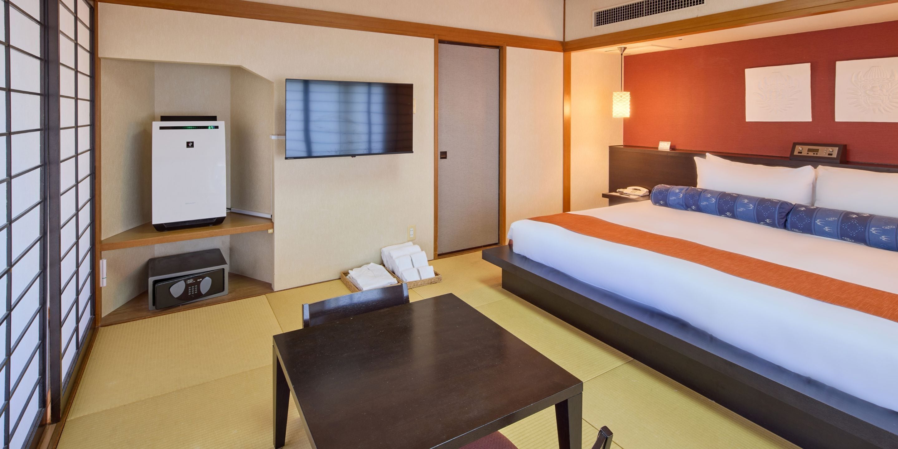 A hotel room with a bed, a desk, a TV, a refrigerator, and a bedside table.