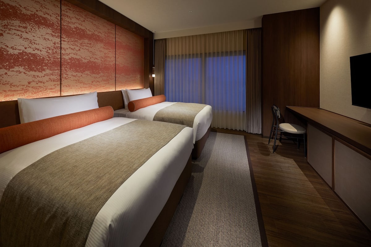 A hotel room with two beds, a desk, and a TV.