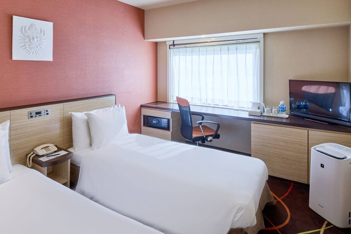 A hotel room with two beds, a desk with a chair, a TV, a phone, and a small heater.