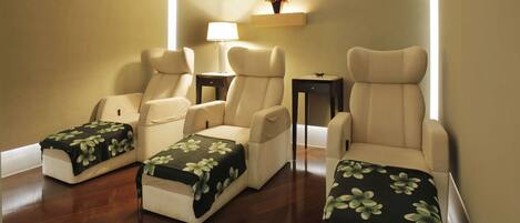 A room with three reclining chairs, a small table with a lamp, and a shelf with a flower arrangement.