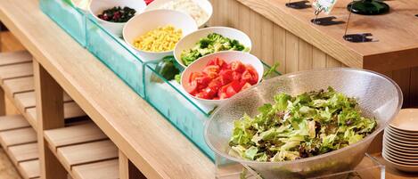 A buffet line with various food items in bowls, including salads, vegetables, and other dishes.