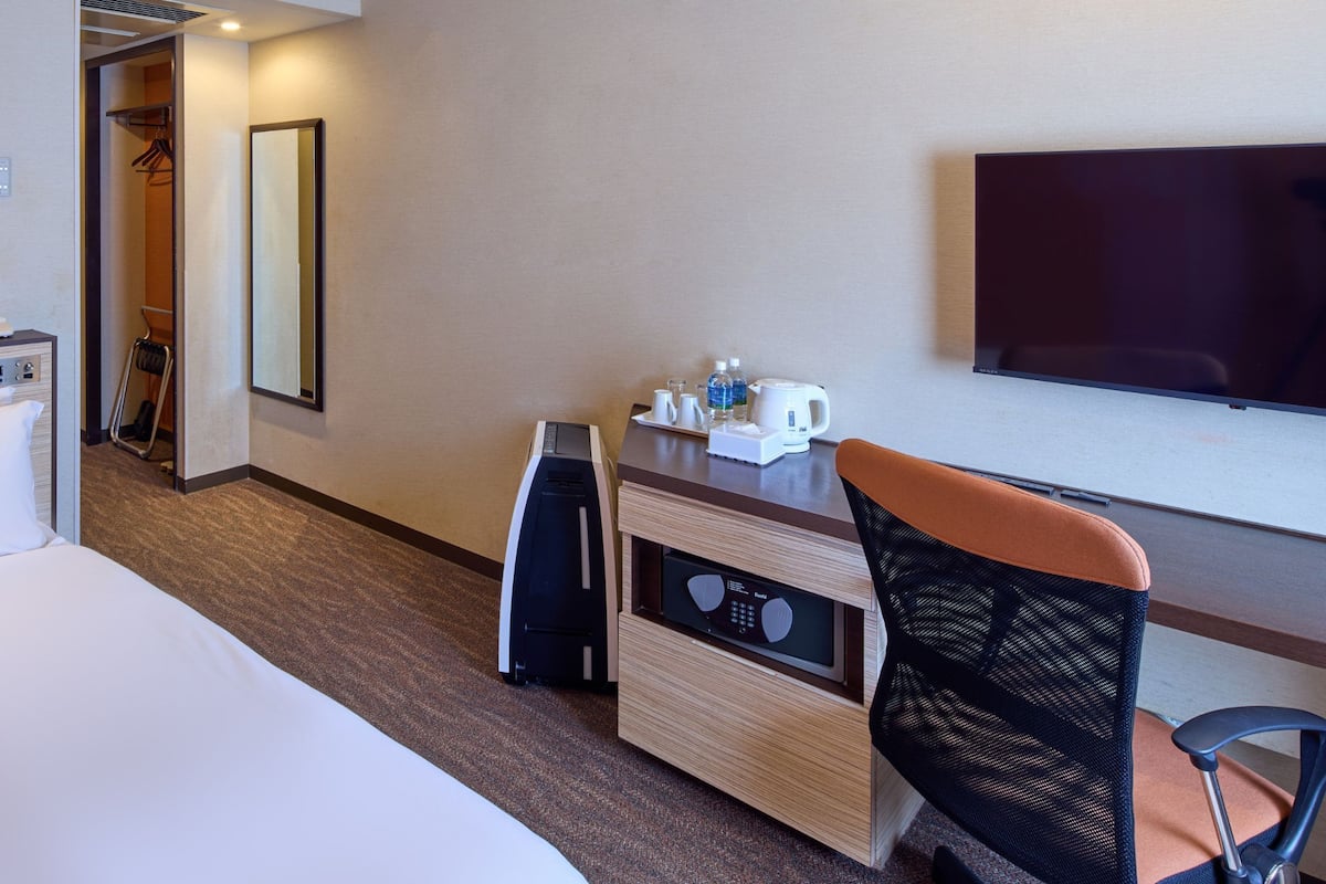 A hotel room with a bed, a desk with a computer, a chair, a TV, and a mirror.